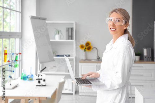 Happy female scientist with sunflowers and laptop working in laboratory