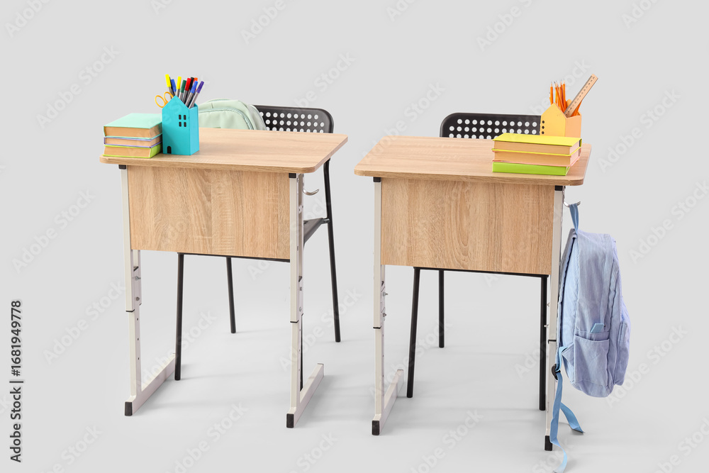 Fototapeta premium Modern school desks with backpacks, books and stationery on grey background
