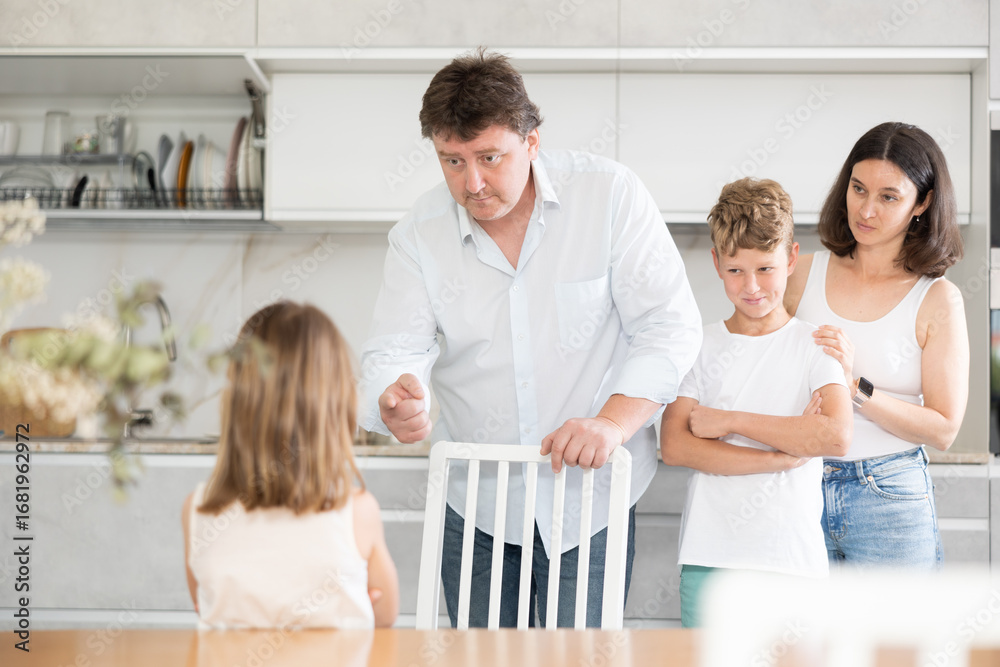 Fototapeta premium Mom and dad scold their guilty daughter standing in kitchen at home