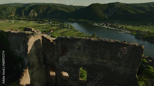 Scenic view from a high hill in Dürnstein, Austria. Ruins of a medieval stone building in the foreground, vineyards, green hills and the Danube River in the valley.