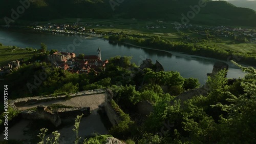 High viewpoint over Dürnstein and nearby towns in Austria. Lush green hills, vineyards, the Danube River and blue sky on a sunny late afternoon before sunset.