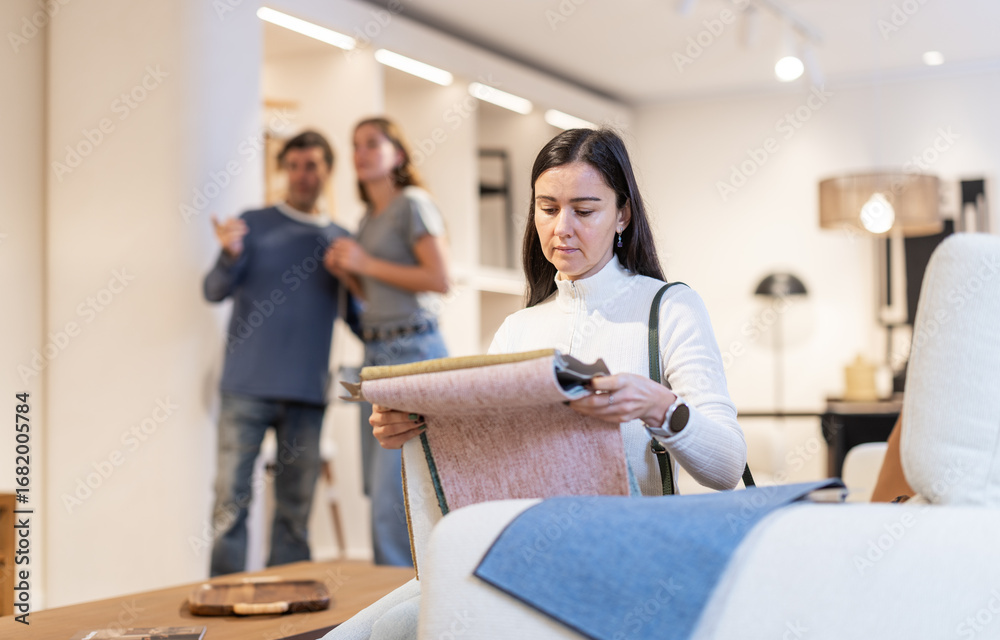 Obraz premium Woman in a European salon is considering textile options for upholstering a sofa in the living room. Buyer is holding examples of upholstery in her hands, she is planning to renovate and buy new