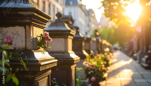 Fototapeta Naklejka Na Ścianę i Meble -  Sunlit cemetery pathway with ornate stone pillars and flowers