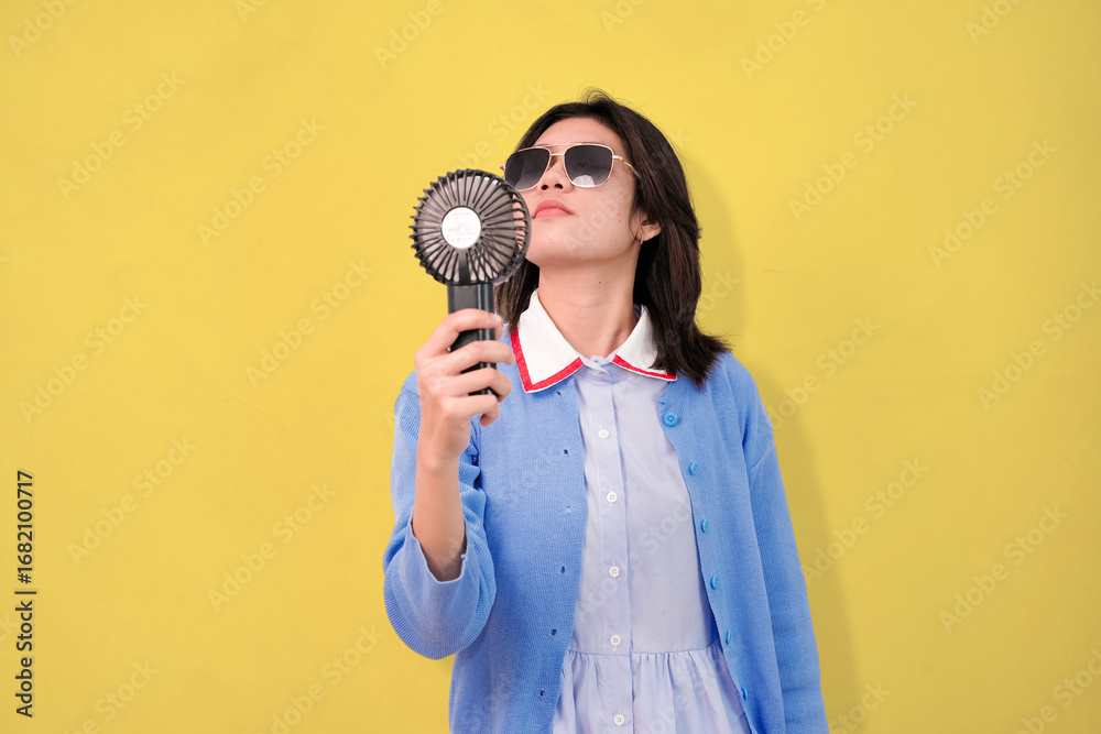 Obraz premium A confident young woman cooling herself with a hand-held fan while wearing sunglasses