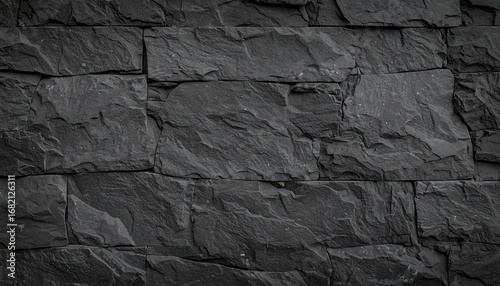 Close-up of a dark gray stone wall, featuring rough, textured surfaces and rectangular blocks arranged in a horizontal pattern