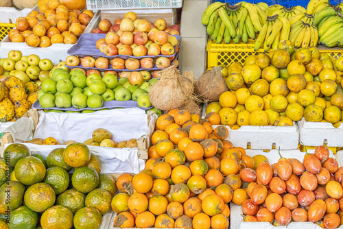 Colorful fresh fruit stand at a local market featuring oranges, tamarillos, coconuts, bananas, red and green apples, dragon fruit, and granadillas. Perfect for themes of tropical nutrition, Ecuadorian