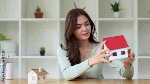 Young woman reviewing house model while deciding on new home. Real estate concept, decision-making process in modern interior.