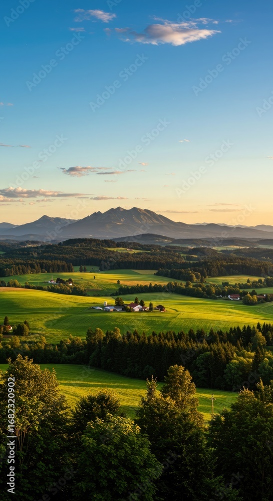 Obraz premium Rolling green hills and farmland at sunset with distant mountains