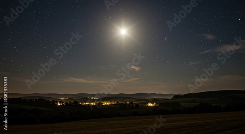 Moonlit rural landscape with a starry sky and distant village lights