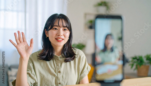 自宅でスマートフォンを使いライブ配信を行う若い女性インフルエンサー、笑顔で視聴者に手を振りながら商品レビューを届ける明るく親しみやすい室内シーン