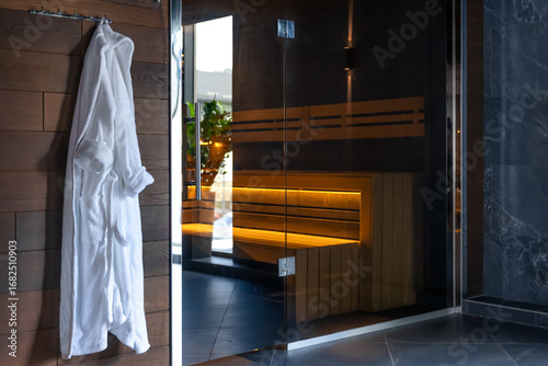 White robe by sauna glass door. Warm spa interior.