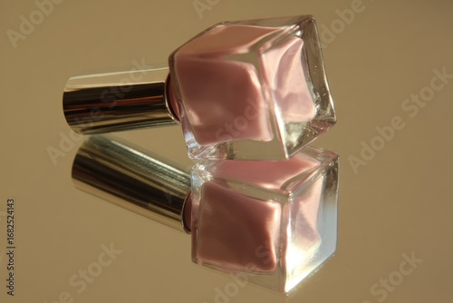Two mauve nail polishes, square bottles, reflected on a gold surface