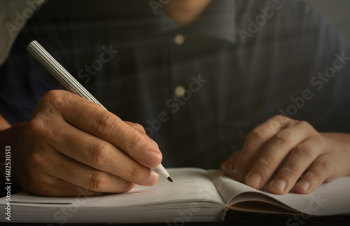 A man is writing a book with warm light. Concept: Education, taking notes, writing a report.