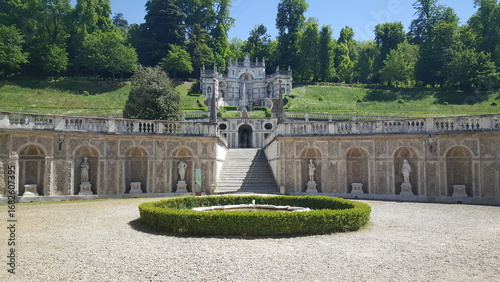 A wide-angle view of the magnificent Reggia di Venaria, showcasing its long Baroque facade, grand royal residence, and formal manicured gardens under a clear blue sky.