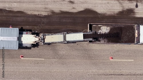 A slow-motion aerial shot of a cold milling machine scraping and removing the top layer of asphalt on a road construction site.