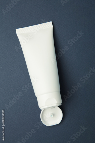 Facial skincare white tube bottle with lid open product on dark blue background. Vertical photo