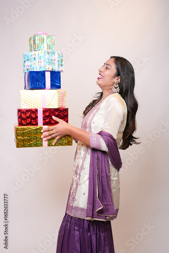 Young indian woman wearing traditional outfit holding gift boxes standing isolated on white studio background. Diwali or festive celebration concept.