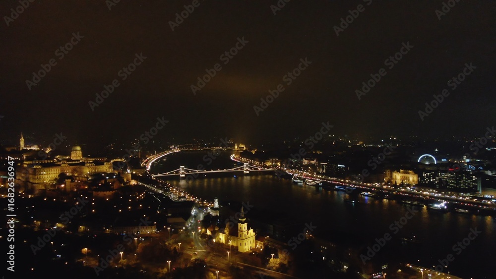 Naklejka premium Picturesque drone view of glowing Budapest city with lights reflecting in channel in night time, Hungary