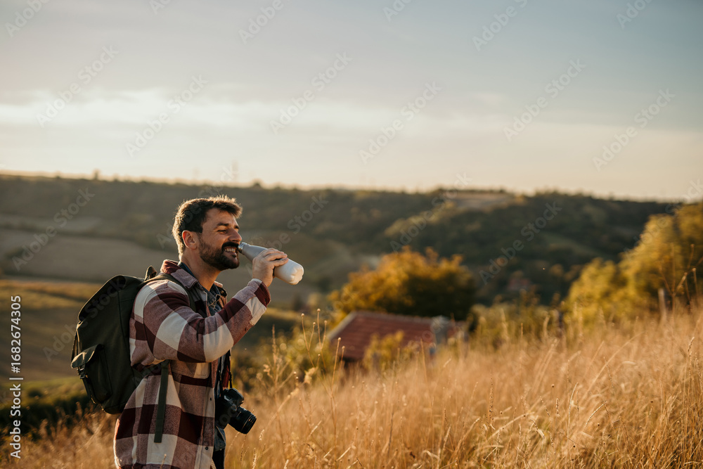 Fototapeta premium Photographer drinking water in a field during golden hour