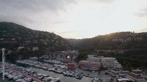 Drone footage captures picturesque marina of Mandelieu La Napoule at sunset. Lush hills framing village create a serene atmosphere in the South of France, highlighting nautical and landscape beauty
