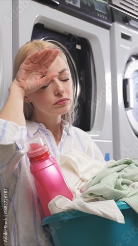 A woman takes a brief moment to reflect while doing laundry, surrounded by several washing machines