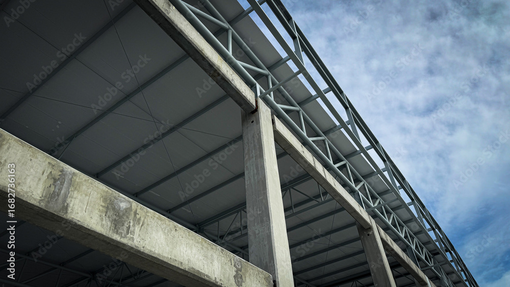Fototapeta premium Concrete column and steel roof truss structure under construction, architectural framework detail with engineering design against blue sky background.