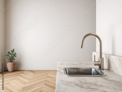A minimalist kitchen corner showcases a modern stainless steel sink and faucet, accented by a muted beige wall and light wooden floors.