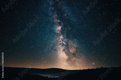 A vast expanse of night sky, dotted with countless stars, showcases a brilliant milky way, stretching across the darkness, and silhouetted mountain ranges.