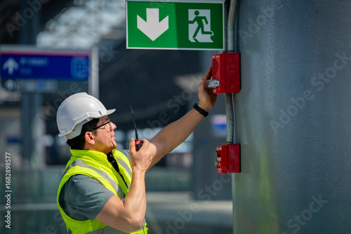 Safety engineer checking fire alarm system public building using a walkie-talkie inspecting emergency equipment an exit sign highlights workplace safety fire prevention and building maintenance.