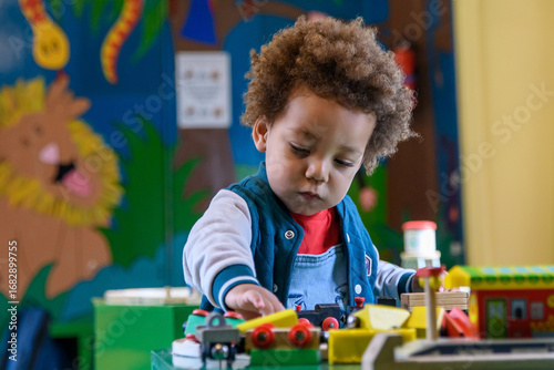 Toddler playing with a train set at nursery, kinder garden. Multi ethnic boy at playtime. 