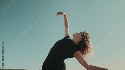 Elegant dancer gracefully moving outdoors with arm extended against a clear blue sky. Concept of freedom, art, and expression.