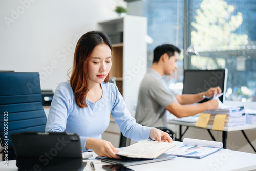 Young beautiful woman typing on tablet and laptop while sitting at the working white table