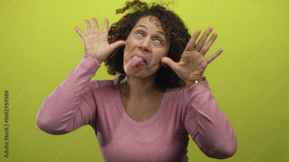 Αυτοκόλλητο Middle aged woman pulls her hands to her ears while sticking out her tongue in a green studio setting; playfulness