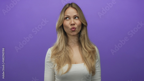 Woman makes fish face with puckered lips and sunken cheeks inside purple studio; playfulness fun humor expression.