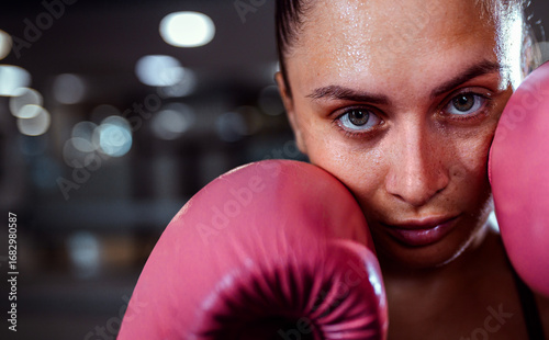 Close up portrait of female boxer in guard position with gloves looking at camera.
