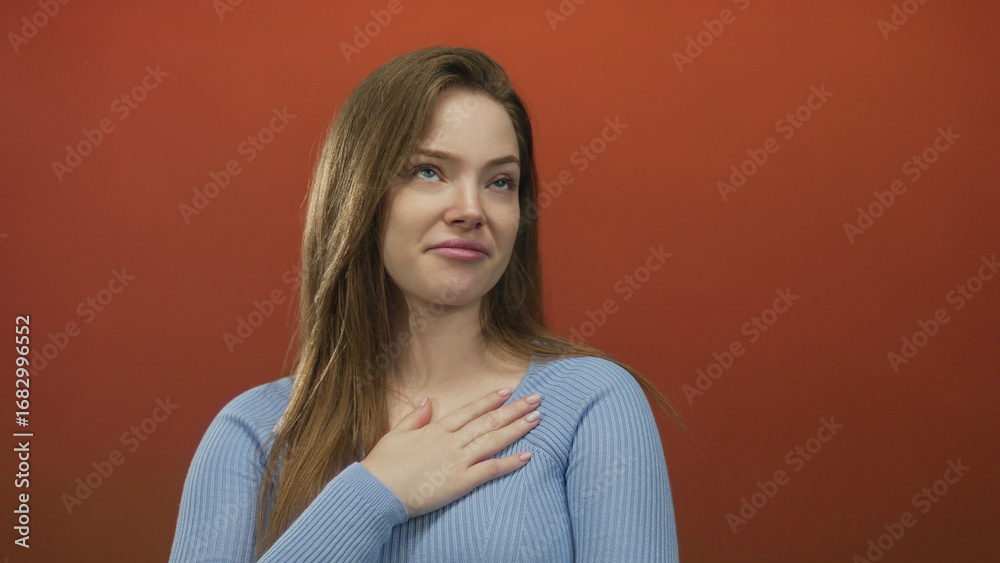 Fototapeta premium Woman looks up in studio wearing blue sweater against red background with calm demeanor; uncertainty.