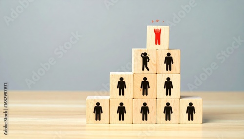 Wooden block pyramid representing a team, with one block topped by a red figure triumphing. A black figure stands behind, perhaps contemplating the leader