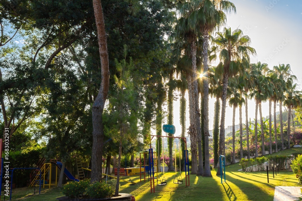 Fototapeta premium Children’s playground among palm trees in Mahmutlar, Alanya, Turkey, sunny summer resort garden with family leisure and vacation lifestyle