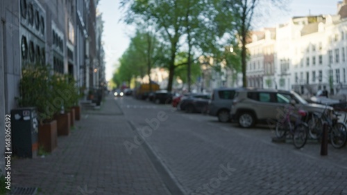 European city street scene with blurred focus showcasing parked cars, bicycles, and cobblestone pavement in a serene residential neighborhood under clear skies.