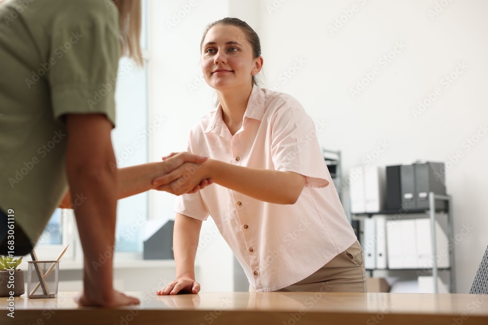 Fototapeta premium Happy women shaking hands at wooden table in office