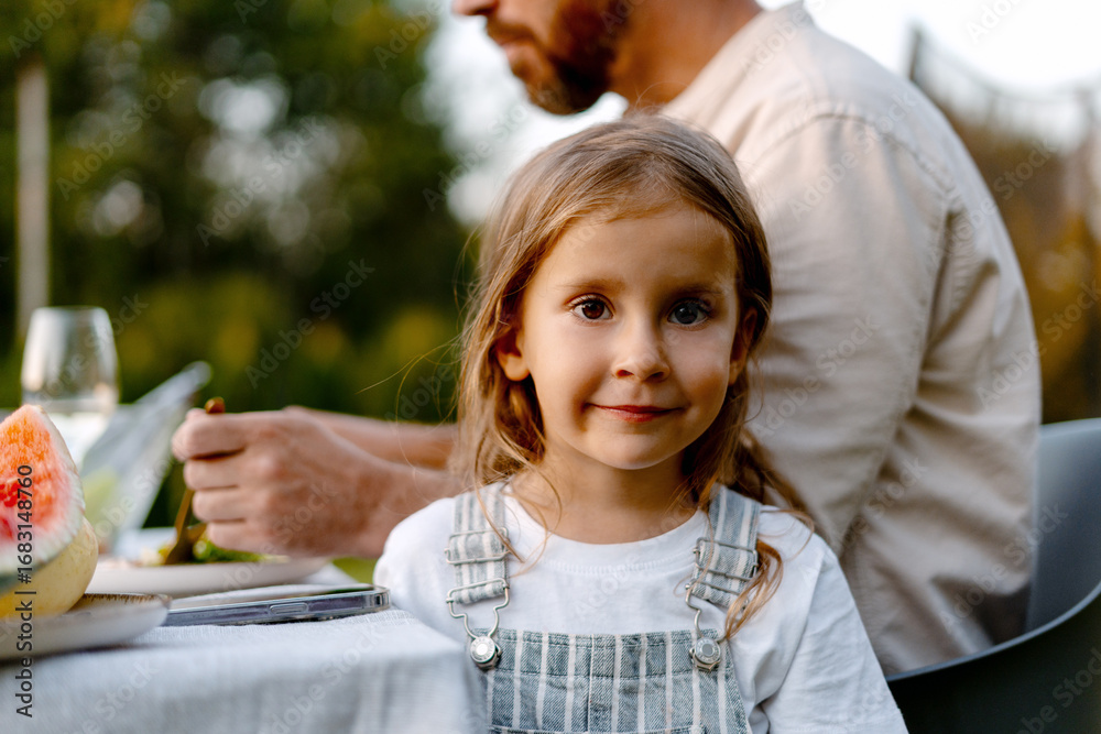 Happy girl enjoying family dinner in garden during summer evening Happy girl enjoying family dinner in garden during summer evening