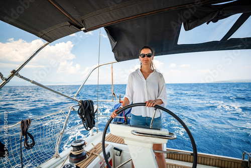 Young woman steering a sailing yacht near Croatia, confidently standing at the helm. Female leadership, empowerment and freedom in maritime lifestyle.
