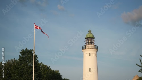 A Coastal Lighthouse stands gracefully at Dusk with a waving Flag, showcasing its charm