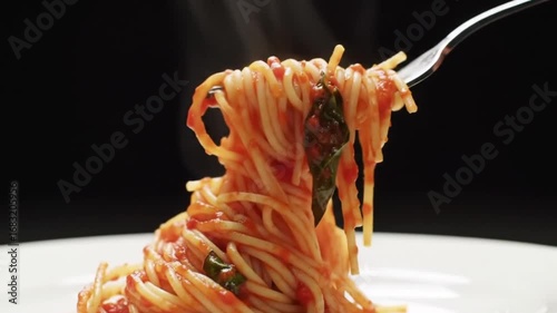 A fork lifts a serving of hot, steaming spaghetti with rich tomato and basil sauce from a white dish against a dark background