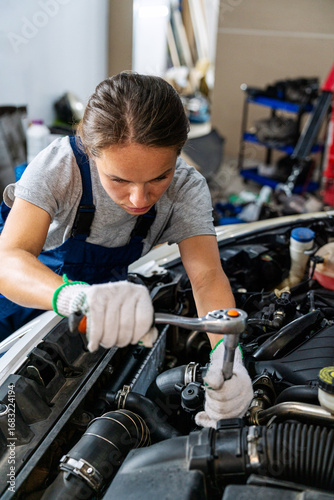 Young woman auto mechanic repairing car at repair garage. Woman at work.