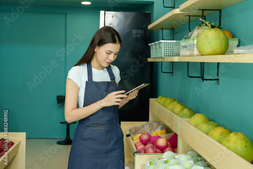 Cuadro en lienzo Asian female shop co-owner using digital tablet checking stock and shelf items i