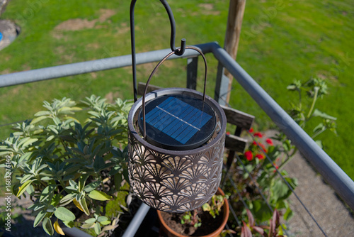 A decorative solar-powered lantern hangs on a balcony, its intricate pattern casting shadows in the sunlight. This image evokes an eco-friendly and stylish outdoor living theme, perfect for home decor