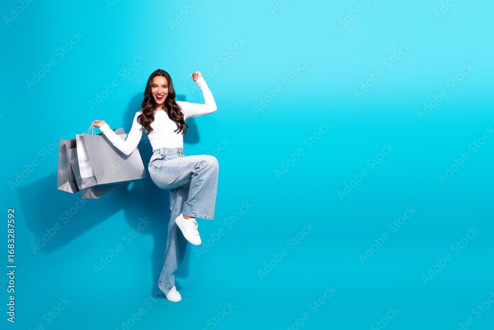 Fototapeta premium Cheerful young woman holding shopping bags against blue background showcasing casual style and joyful expression