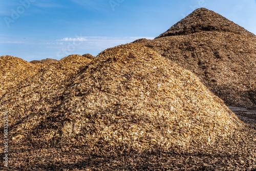 Large piles of wood chips and biomass for renewable energy and mulch production under blue sky in industrial storage area