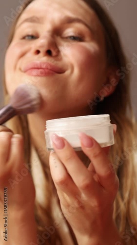 A young woman applies makeup to enhance her features while sitting comfortably in a softly lit room. She demonstrates techniques for achieving a radiant complexion.